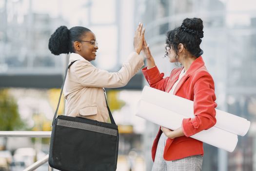 Two women professionals greet each other with a high-five outdoors, showcasing teamwork.