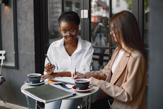Two professional women engaged in a collaborative meeting at an outdoor cafe table.