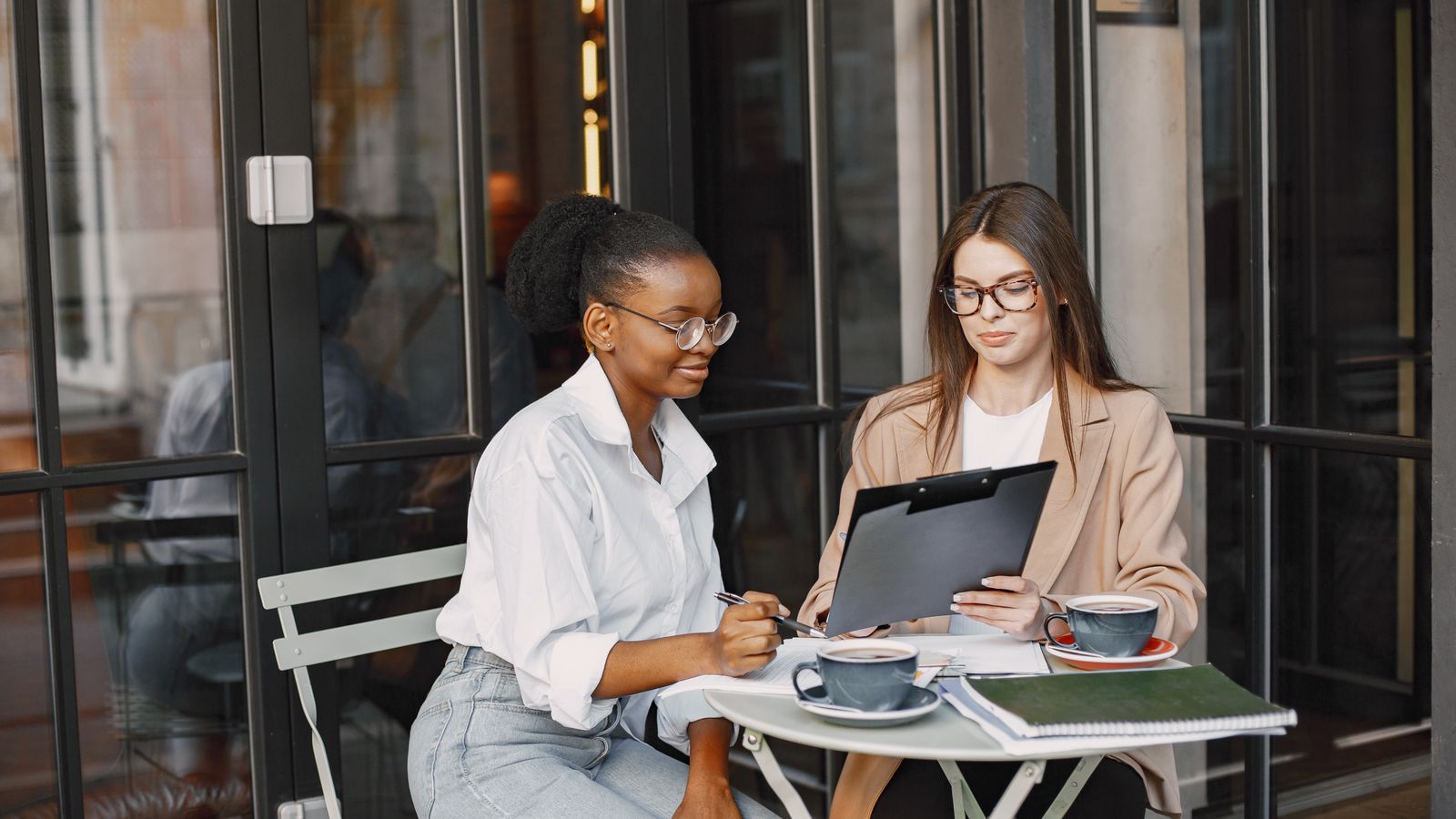Two people with a clipboard and coffee at an outdoor table