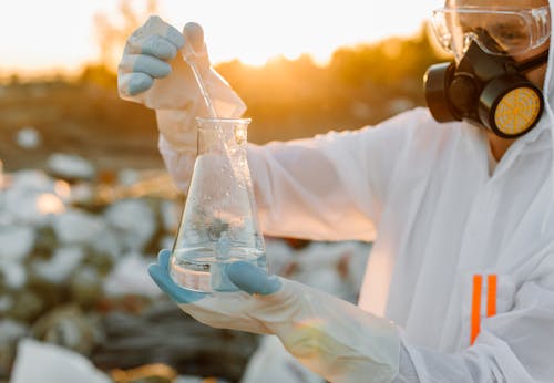 Person in PPE on a Dumpsite holding an Erlenmeyer Flask