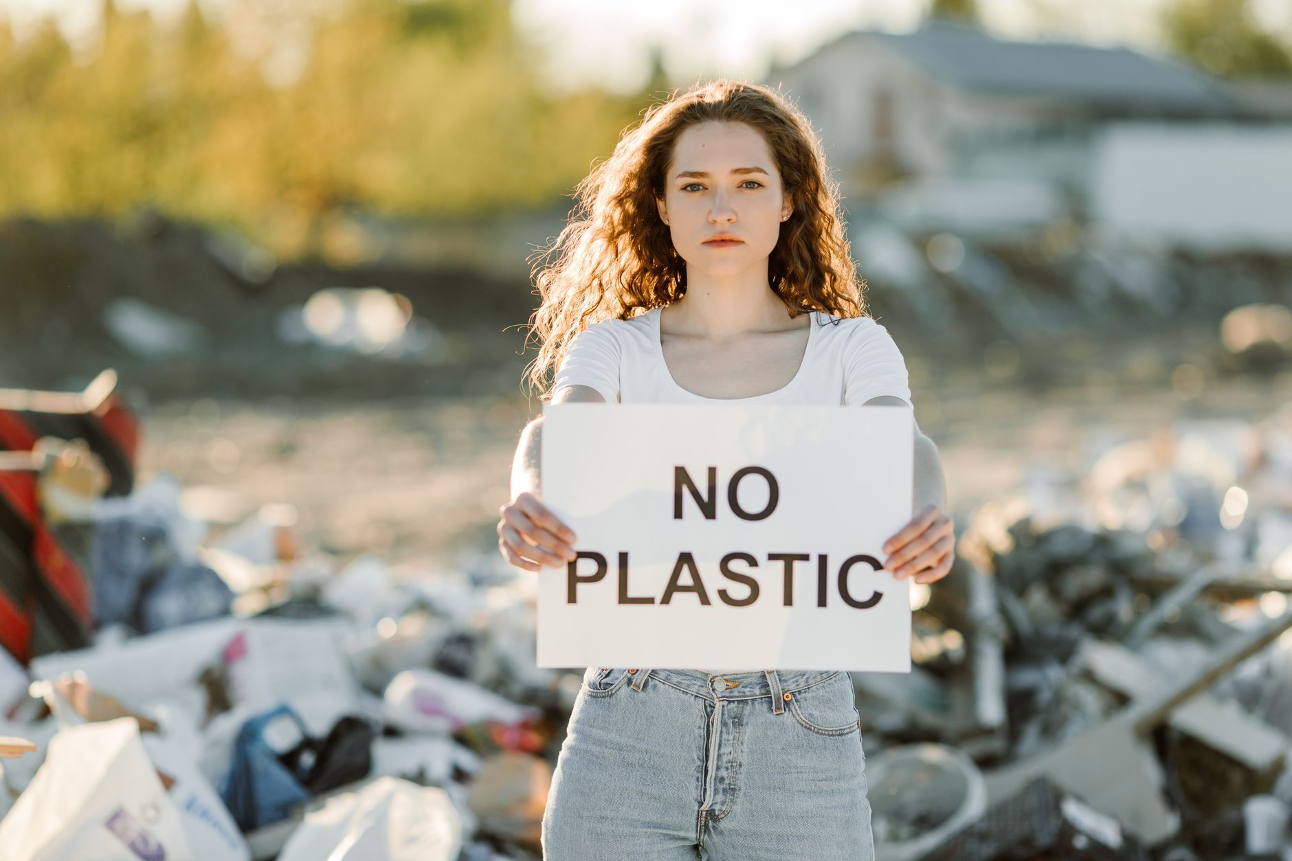 Young woman holding 'No Plastic' sign at landfill, advocating against pollution.