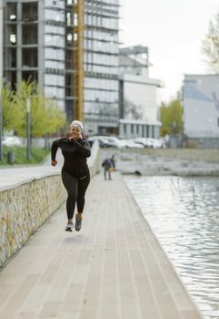 Energetic woman jogging along a waterfront boardwalk with modern buildings in the background.