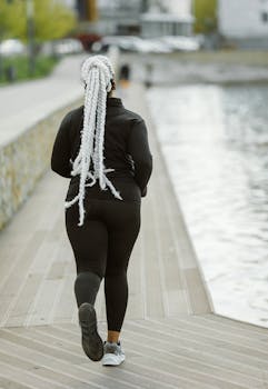African American woman with long braids jogging along a riverside path, embracing a healthy lifestyle.
