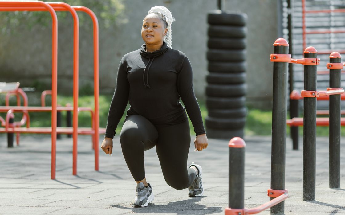Woman in black activewear doing a lunge exercise at an outdoor fitness park