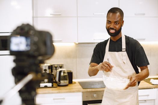 African American man whisking ingredients for a cooking video in a modern kitchen.