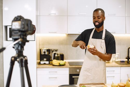 Free A vlogger preparing food in a modern kitchen, recording with a camera. Stock Photo