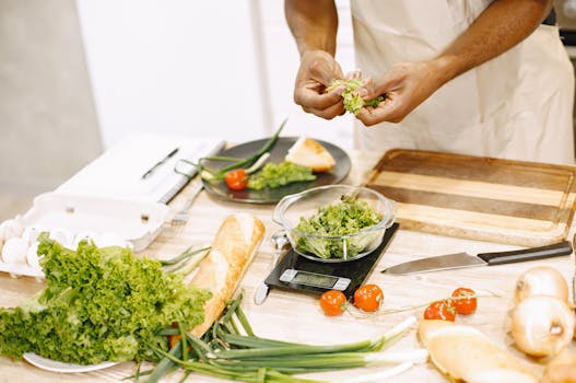 Person preparing fresh salad with tomatoes and baguette in kitchen setting.