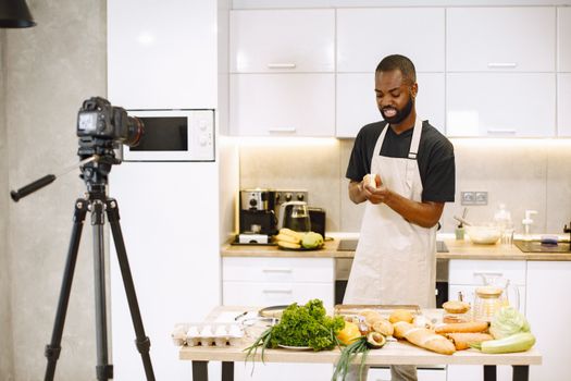 A man prepares food in a kitchen while recording a cooking video.