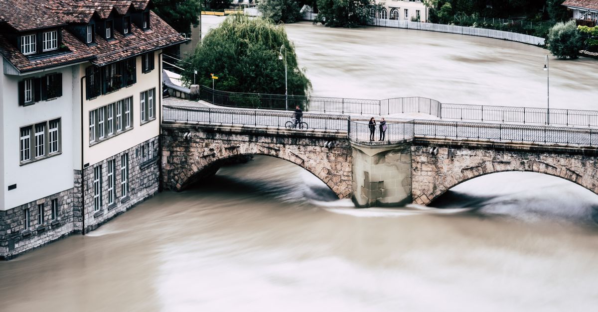 Drohnenaufnahme einer ĂĽberfluteten Stadt mit historischer BrĂĽcke ĂĽber einen ĂĽber die Ufer getretenen Fluss in Bern, Schweiz.