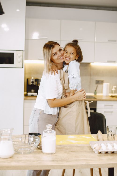 Free Mother and daughter happily embracing amidst baking in a bright kitchen setting. Stock Photo
