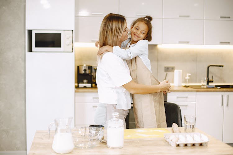 Mother And Daughter Embracing While Cooking Together In The Kitchen