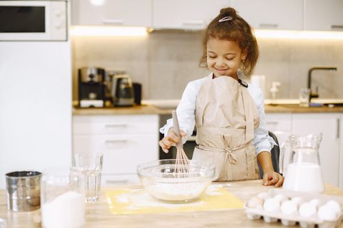 Free Young girl smiling while baking in a kitchen, mixing ingredients in a bowl. Stock Photo