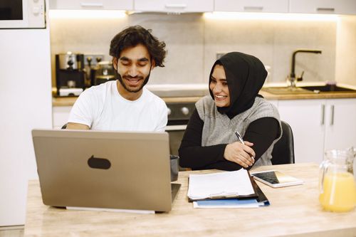 Free Two people collaborating at a laptop in a cozy kitchen setting with documents and juice on the table. Stock Photo