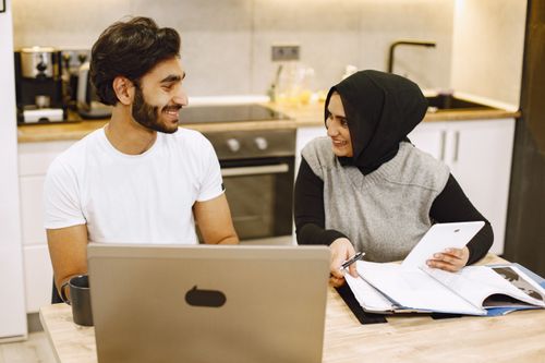 Free Two adults engage in a positive discussion using technology and notes in a kitchen. Stock Photo