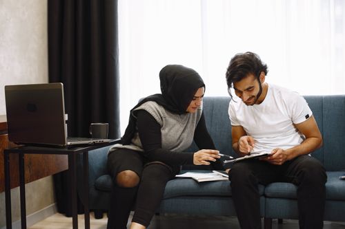 Free Two colleagues discussing a project on a couch with a laptop and documents. Stock Photo