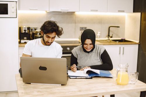 Free Man and woman studying with laptop and documents in modern kitchen. Stock Photo