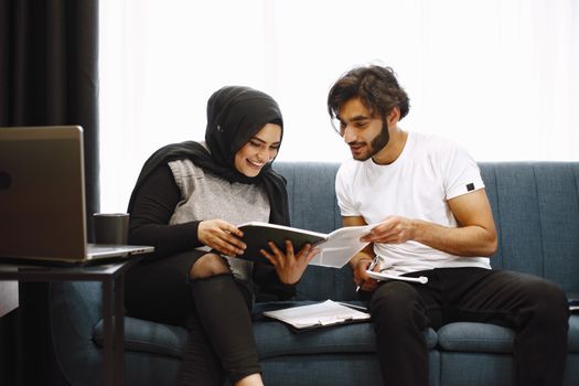 Young couple engaged in reading and studying together on a comfortable sofa indoors.