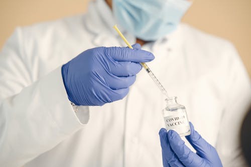 Person Holding Yellow Syringe and Clear Glass Bottle