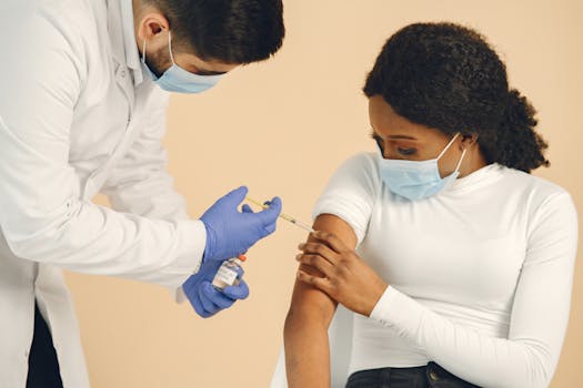 A healthcare professional giving a vaccination to a seated woman, both wearing masks.