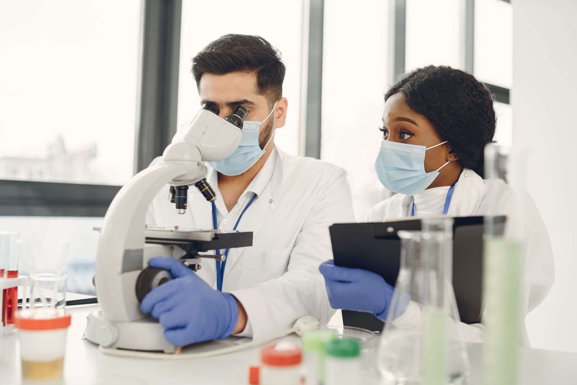 Researchers using a microscope and taking notes in a modern lab.