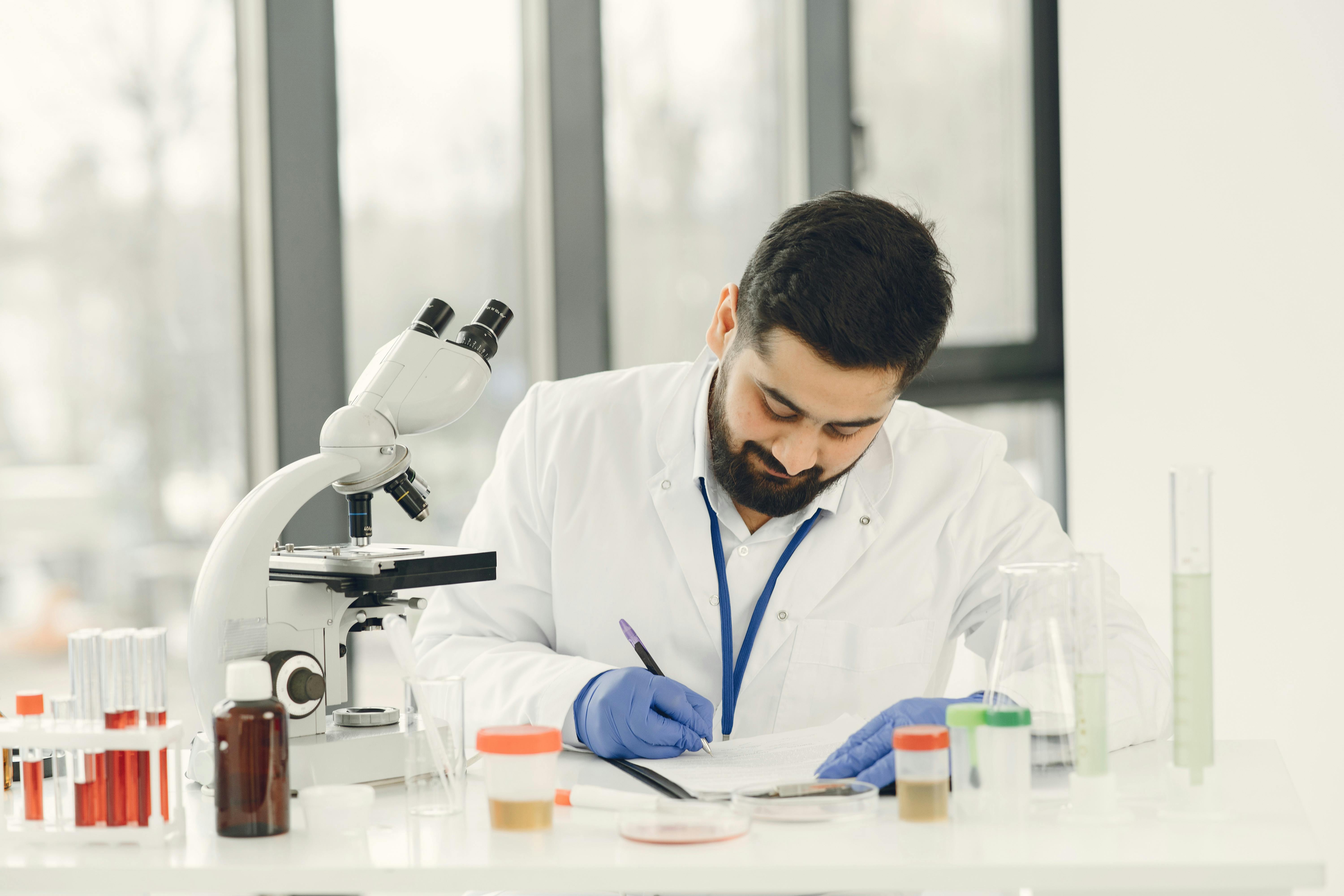 Man Writing on a Notebook Beside a Microscope