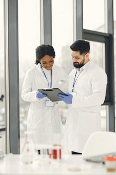 Two scientists in lab coats discussing research on a tablet in a modern laboratory setting.