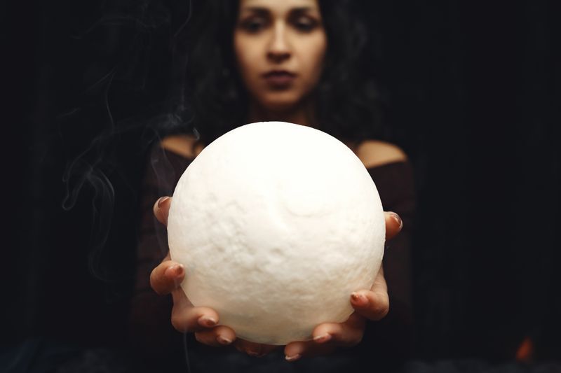 A woman holds a glowing orb with smoke in a mystical atmosphere