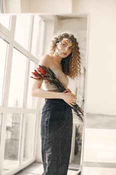 A fashionable woman holding exotic flowers in a bright indoor setting, emphasizing beauty and elegance.
