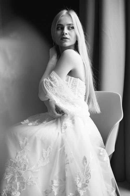 Free Black and white portrait of a woman in a lace wedding dress posing on a chair, exuding elegance. Stock Photo