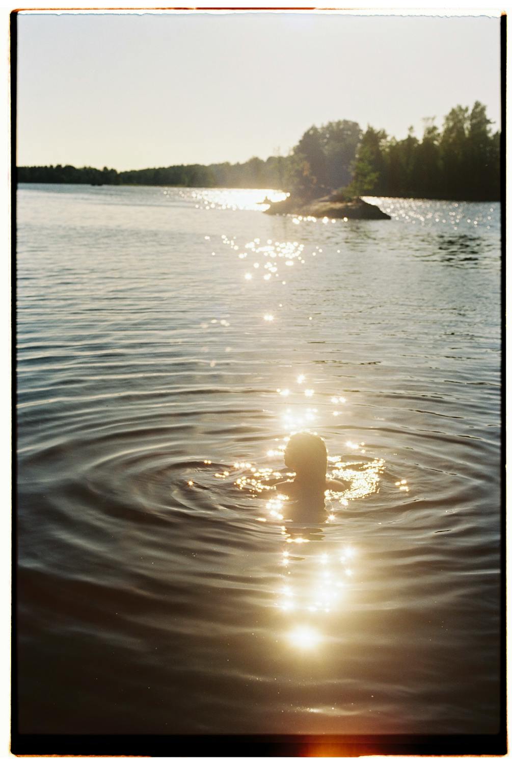 young woman swimming in a lake at sunset