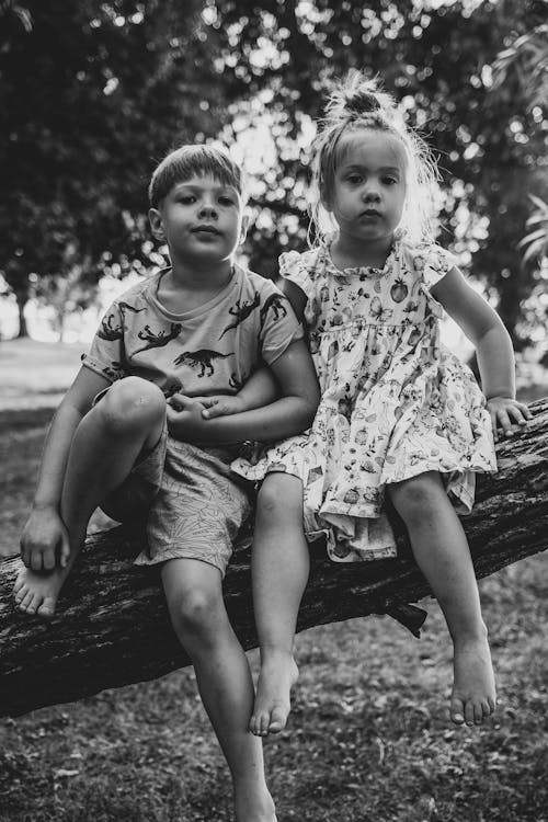 Grayscale Photo of Children Sitting on Tree Trunk