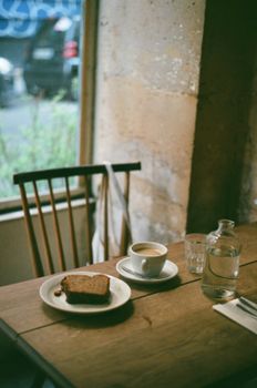 Warm cafe setting with coffee and pastry on a wooden table by a window.