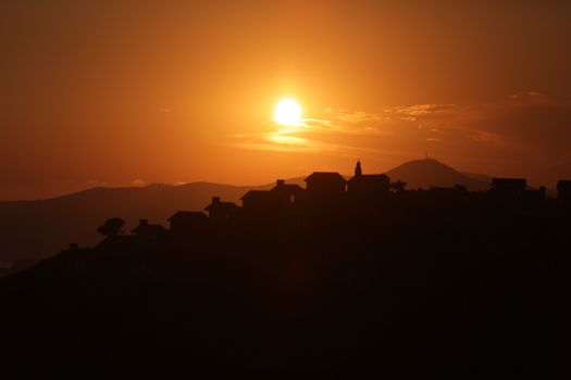 A striking silhouette of houses against a vibrant golden sunset sky.