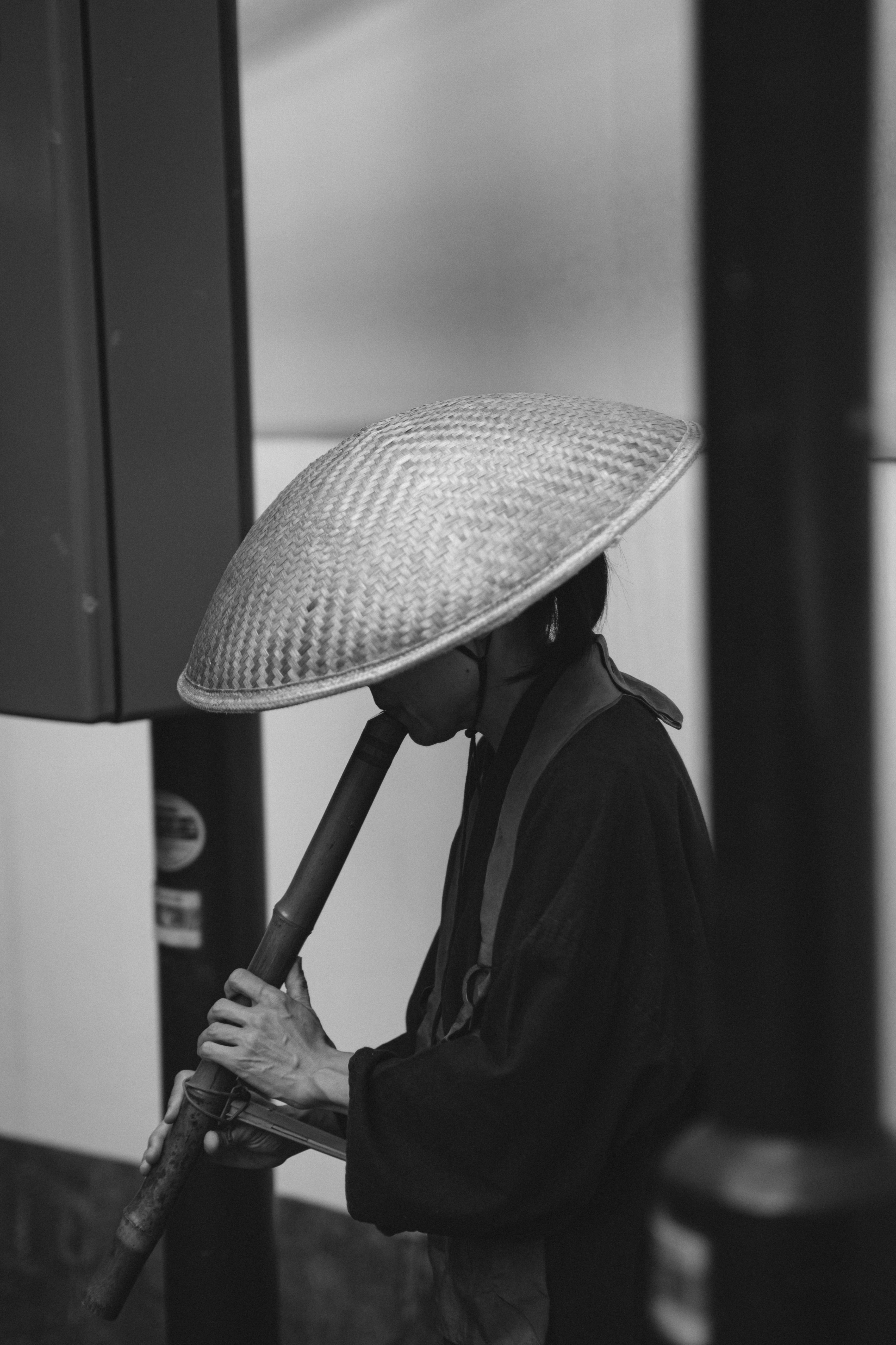 A person playing a flute, wearing a traditional straw hat, in a monochrome setting.