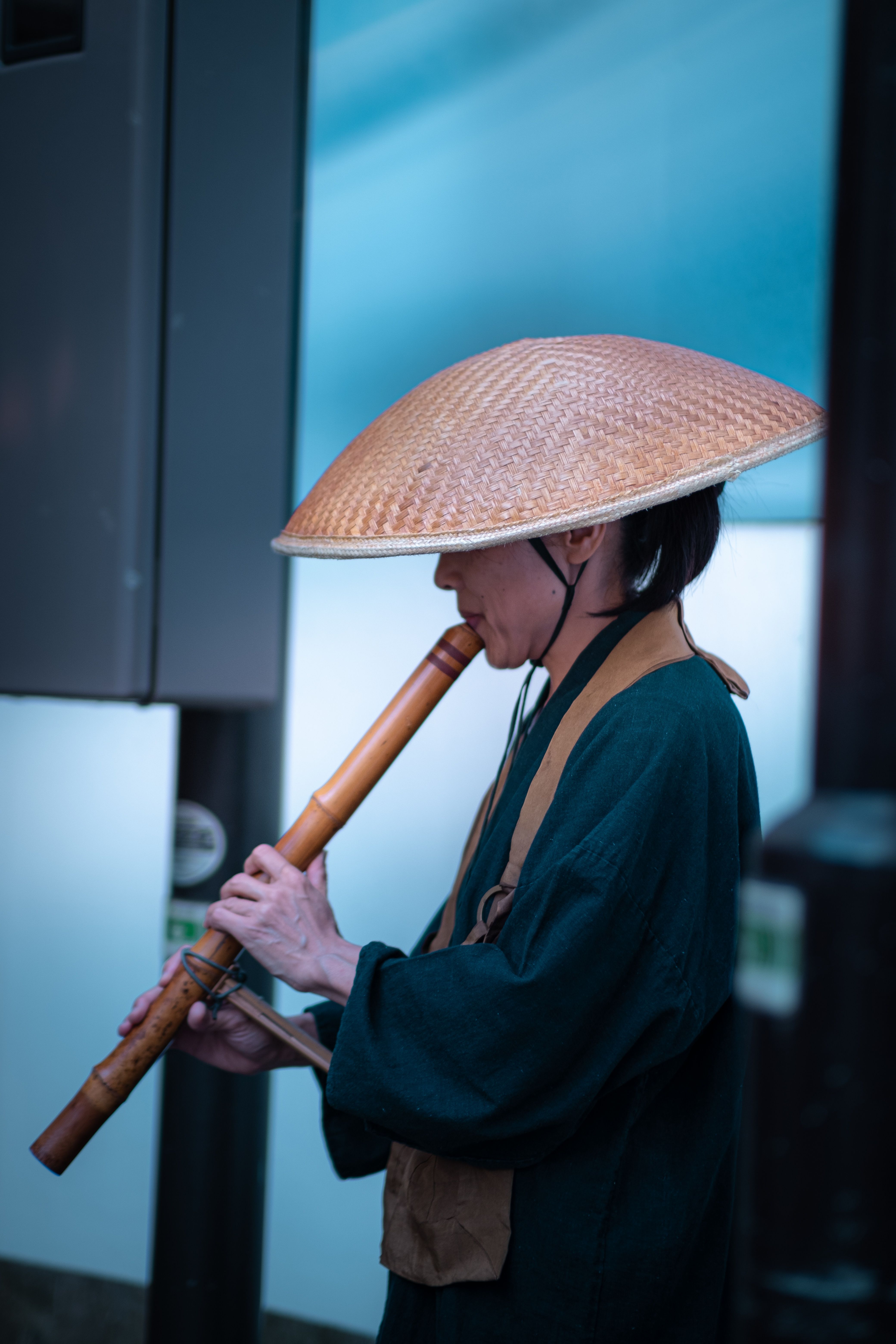 A person in a traditional outfit playing a bamboo flute, wearing a straw hat.