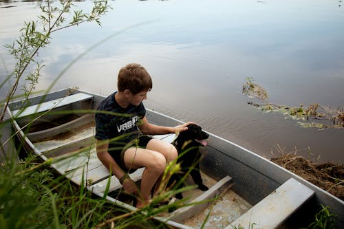 A Young Boy Sitting on a Wooden Boat with His Dog