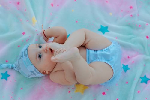 Free Cute baby in a blue outfit playing on a colorful star-patterned blanket. Stock Photo
