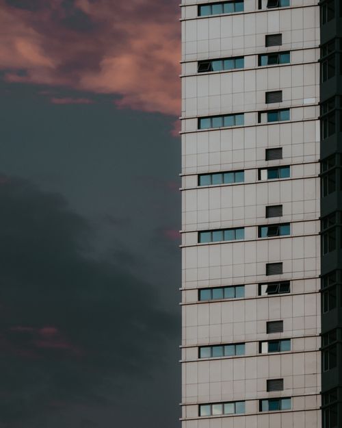 Free A striking modern high-rise building with a dramatic cloudy sunset sky backdrop. Stock Photo