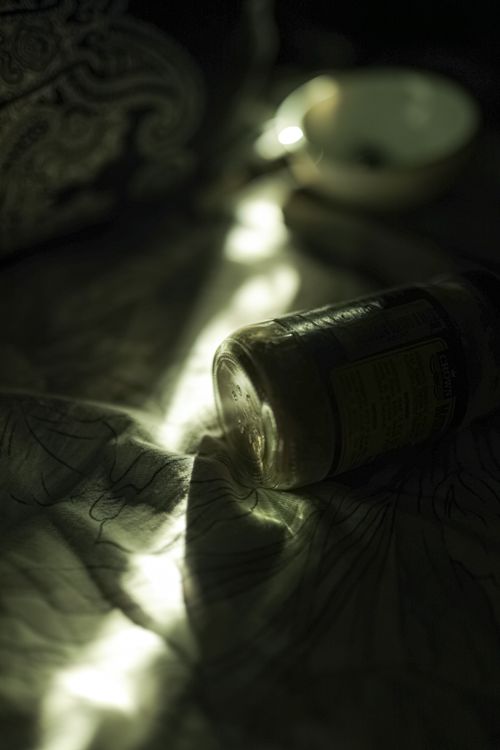 Free Overturned glass bottle on white crumpled tablecloth on table with bowl in murk kitchen with ray of light at home Stock Photo