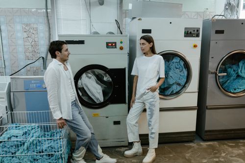 Free Two young adults have a conversation in a modern laundry facility, surrounded by washing machines. Stock Photo