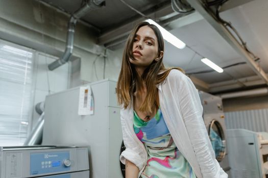 A fashionable woman posing in a contemporary laundry setting with washing machines.