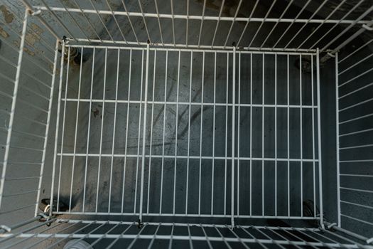 Top-down view into an empty metal shopping cart on a concrete floor.
