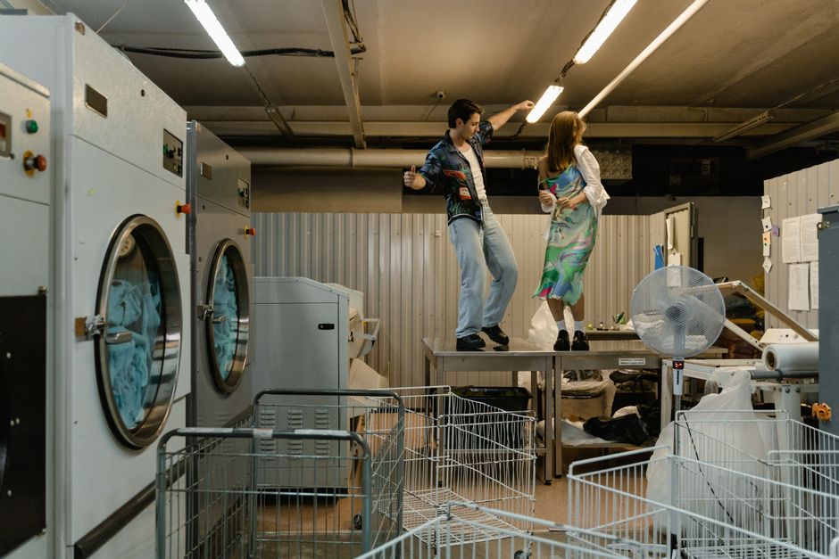 A man and woman dancing joyfully on a table in an industrial laundry room.