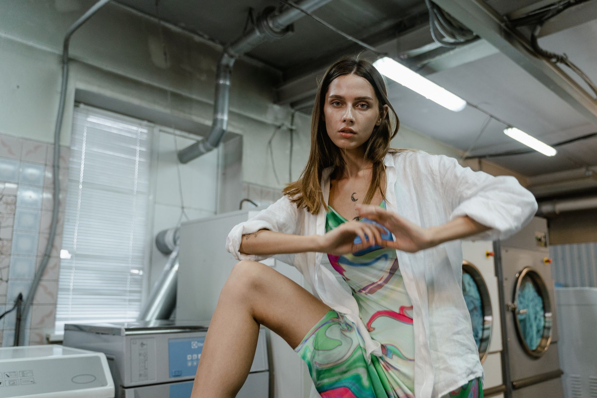 Woman in White Button Up Shirt and Floral Dress Standing Near Washing Machines