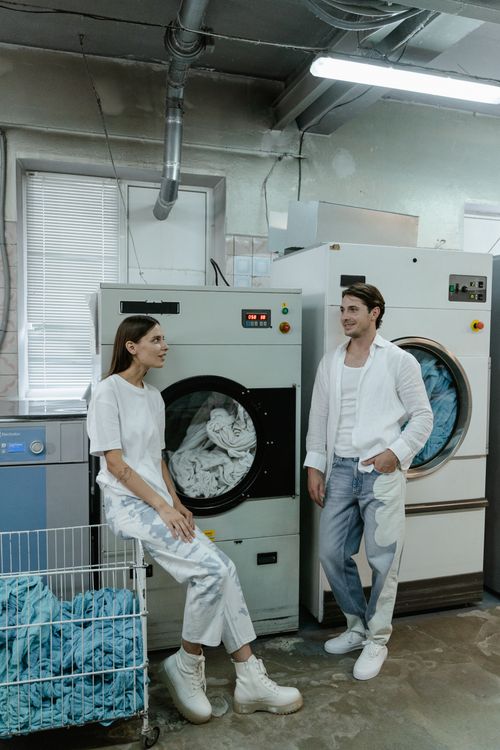 Free Two people in white clothing converse beside industrial laundry machines in a facility. Stock Photo