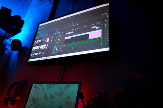 A dark room with computer screens displaying video editing software, creating a moody atmosphere.