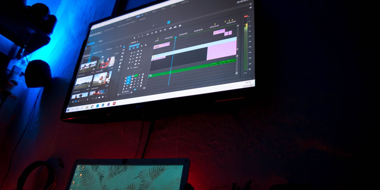 A dark room with computer screens displaying video editing software, creating a moody atmosphere.