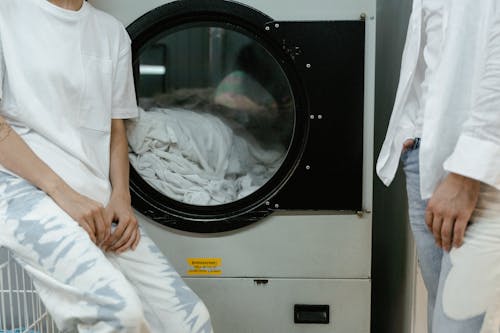 Free People Wearing White Tops near a Washing Machine Stock Photo