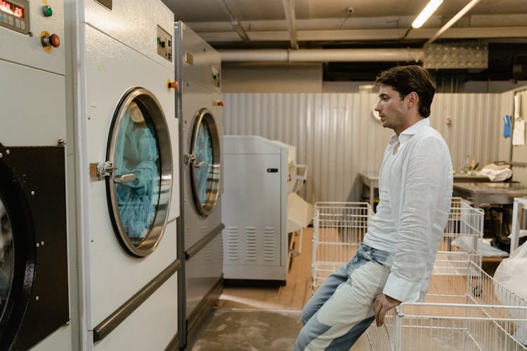 A Man Waiting For His Clothes In A Self-Service Laundry