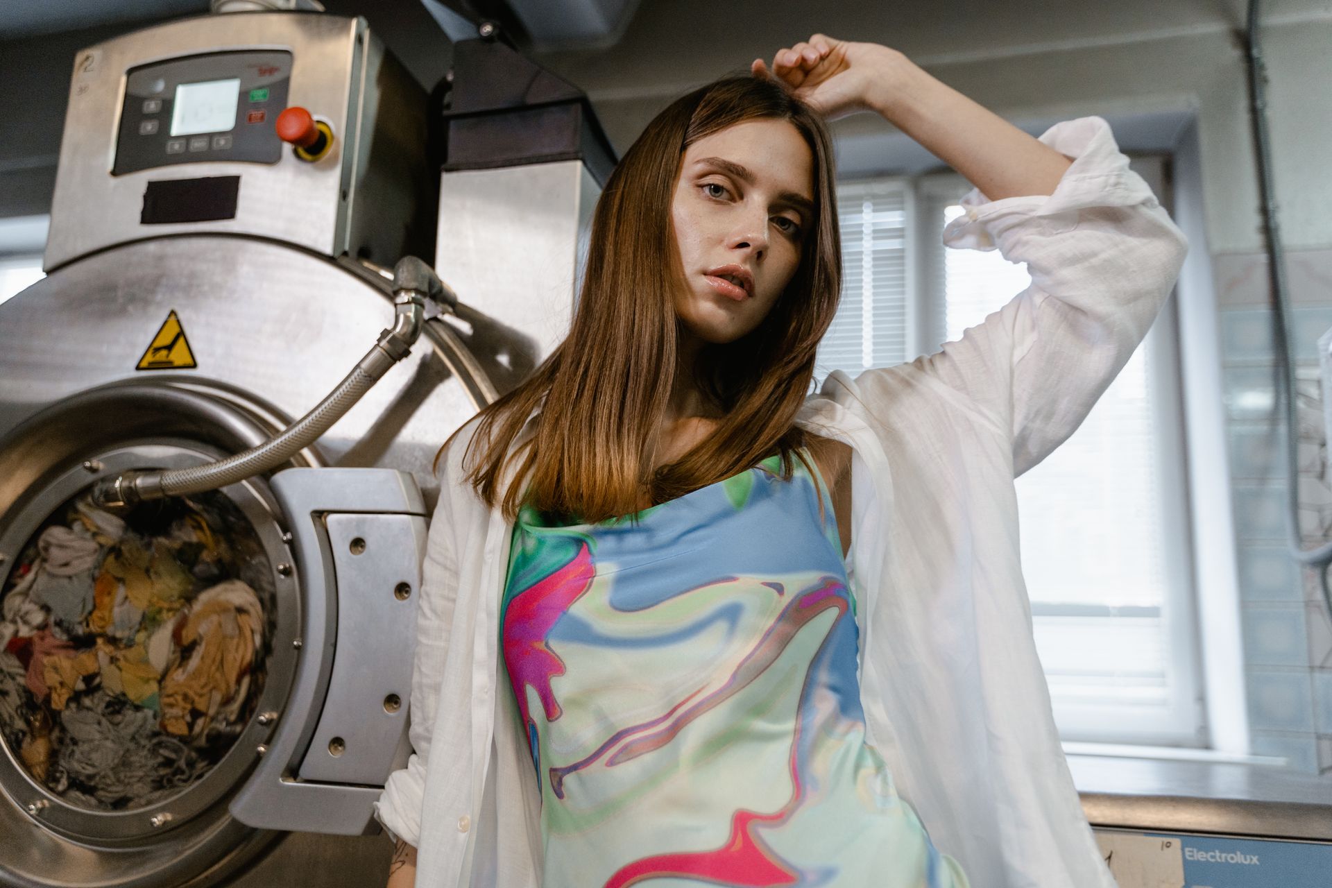 Stylish woman posing next to a large industrial washing machine indoors.
